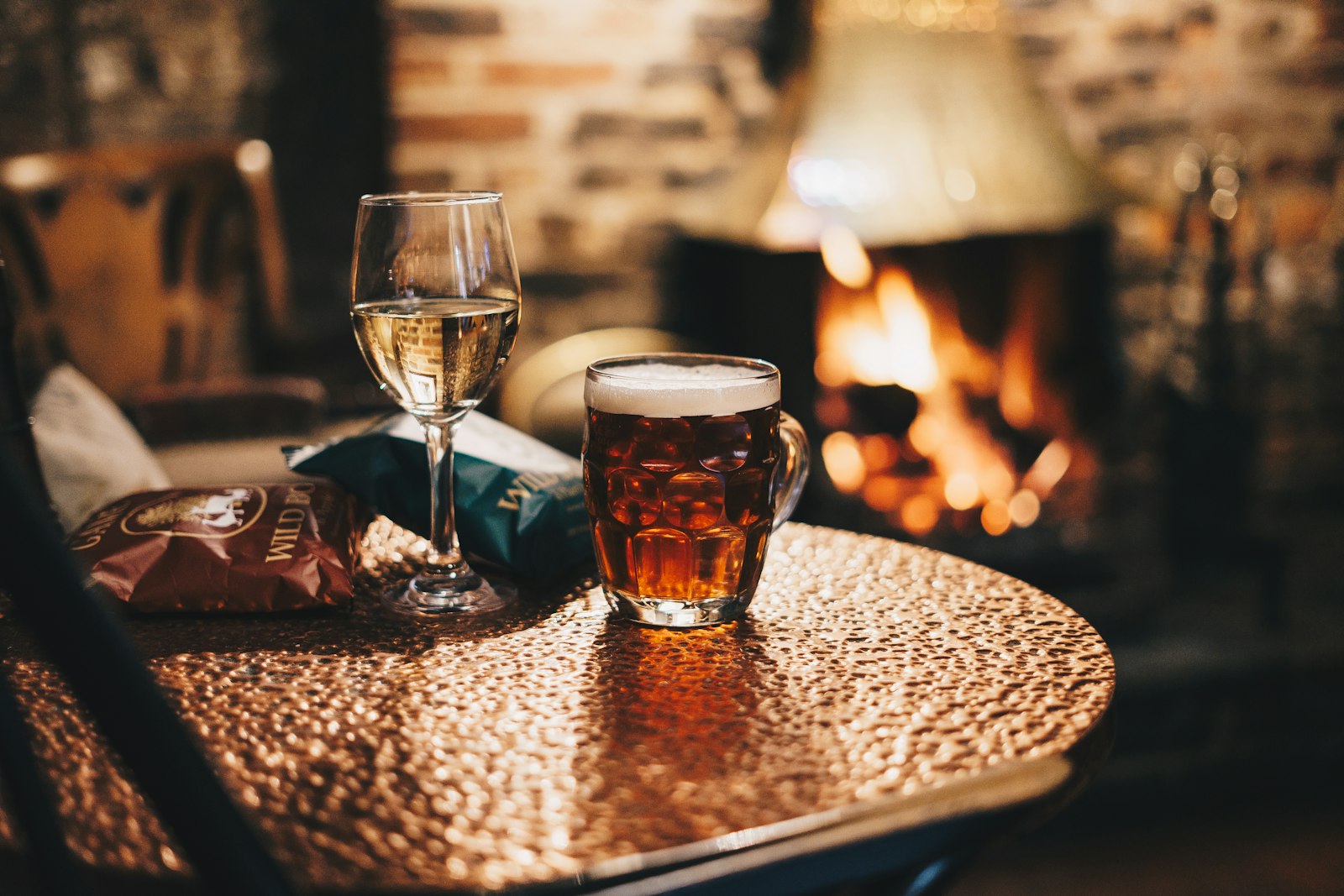 A cosy British pub fireside with a steaming hot toddy and a bowl of spiced wassail on a wooden table.