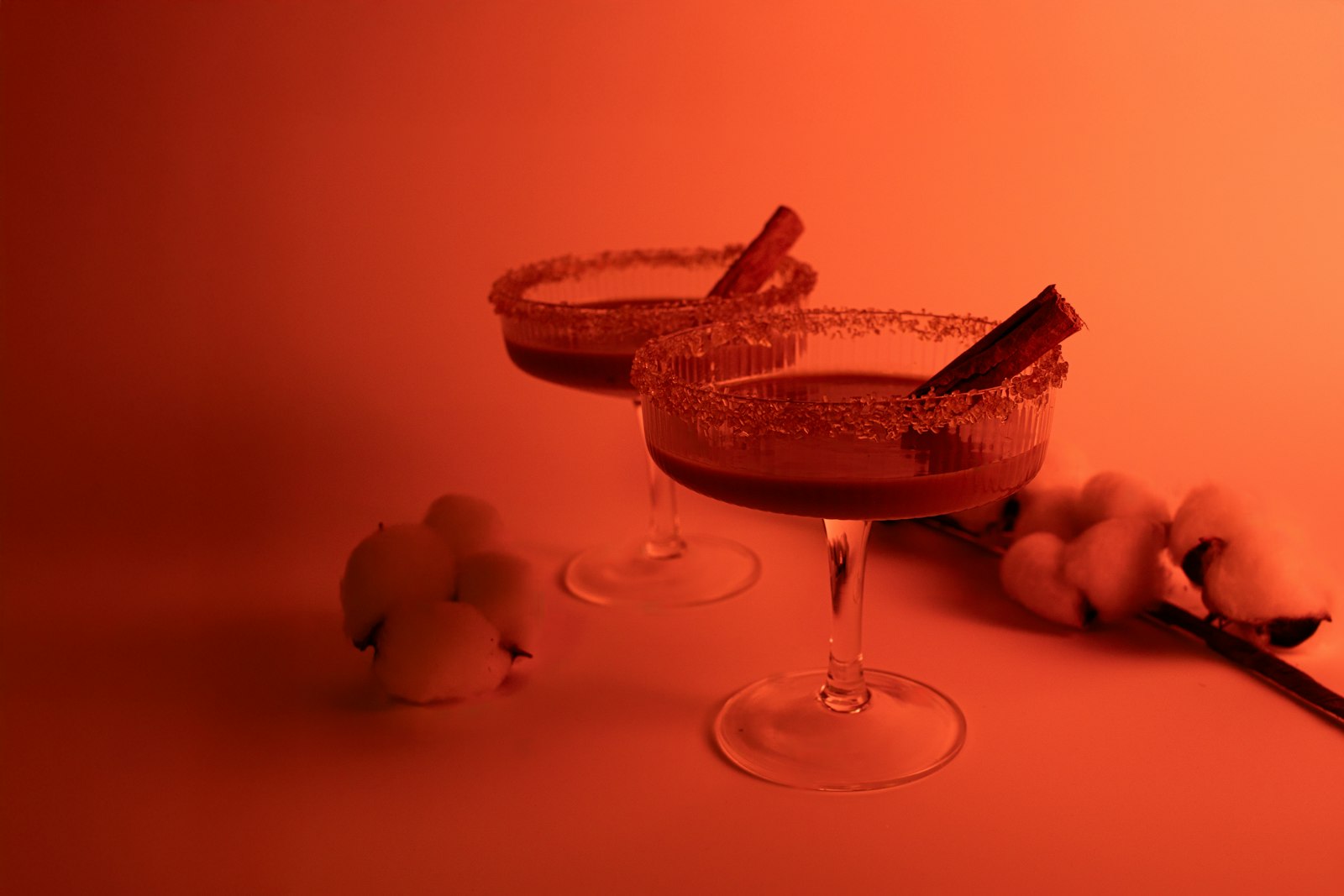 A glass of glögg with raisins and almonds beside cinnamon and cardamom.
