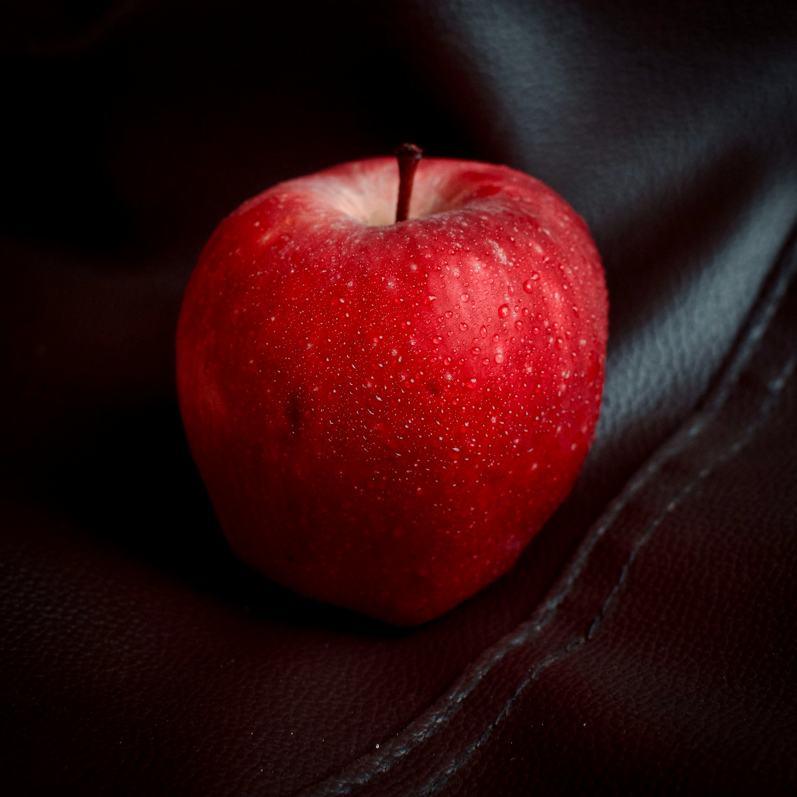 A halved red apple beside whole apples and a glass of cloudy apple juice
