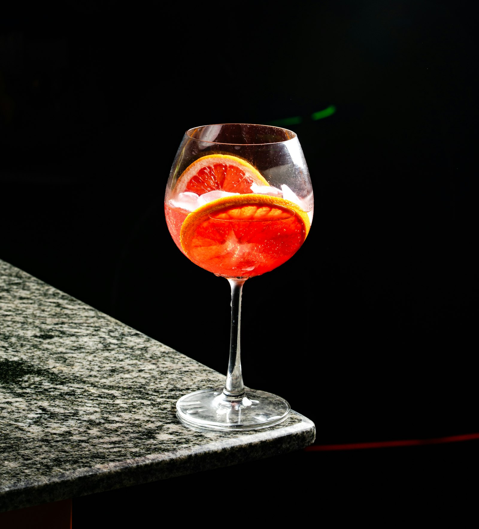 A bottle of gin beside a coupe glass and a sprig of juniper berries