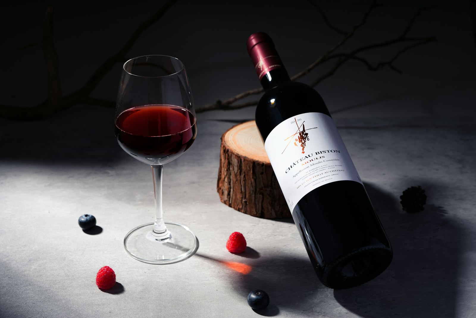 A glass of red wine beside a bottle and scattered winter spices