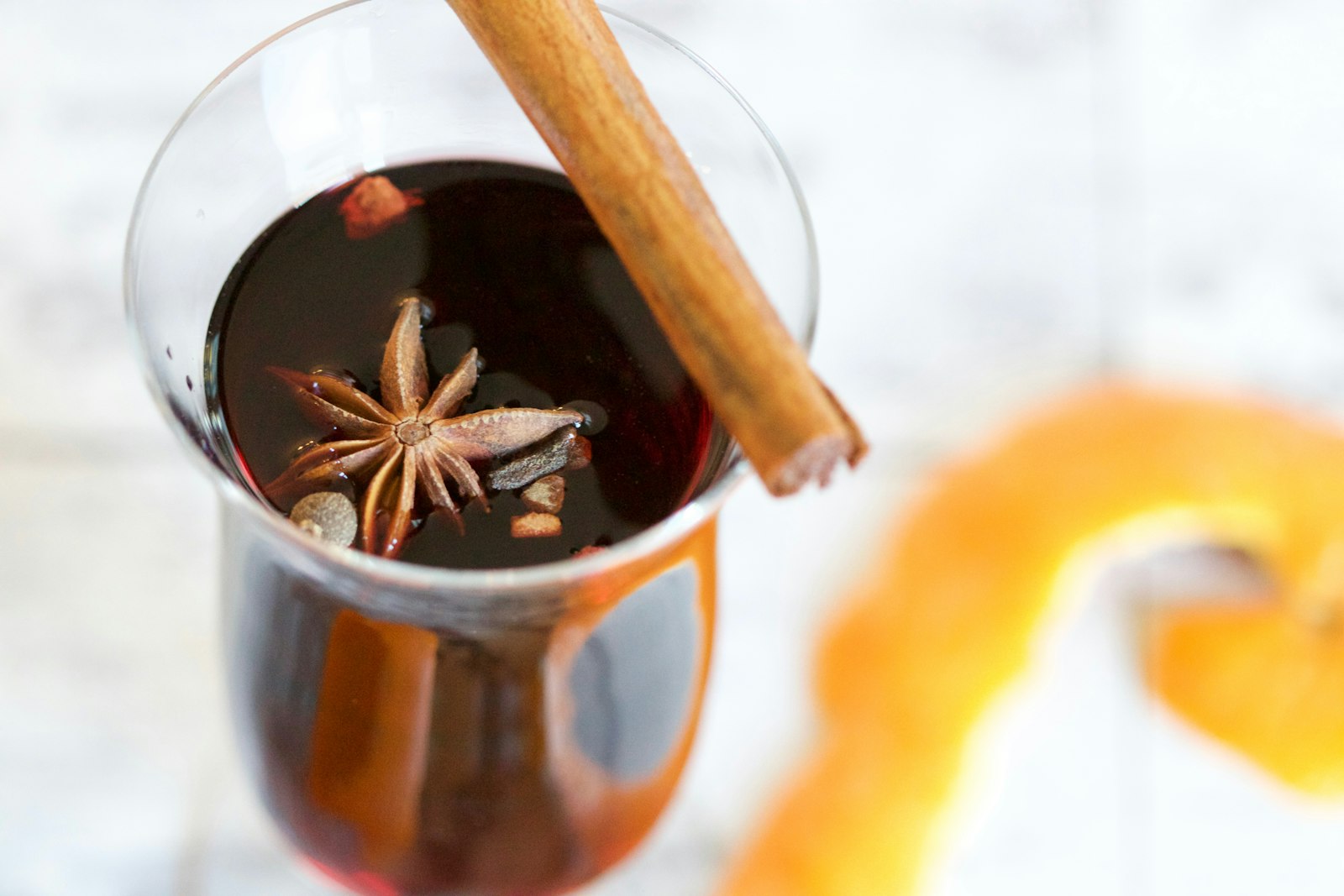 A glass of warm Dutch bisschopswijn beside a clove-studded orange and cinnamon sticks.
