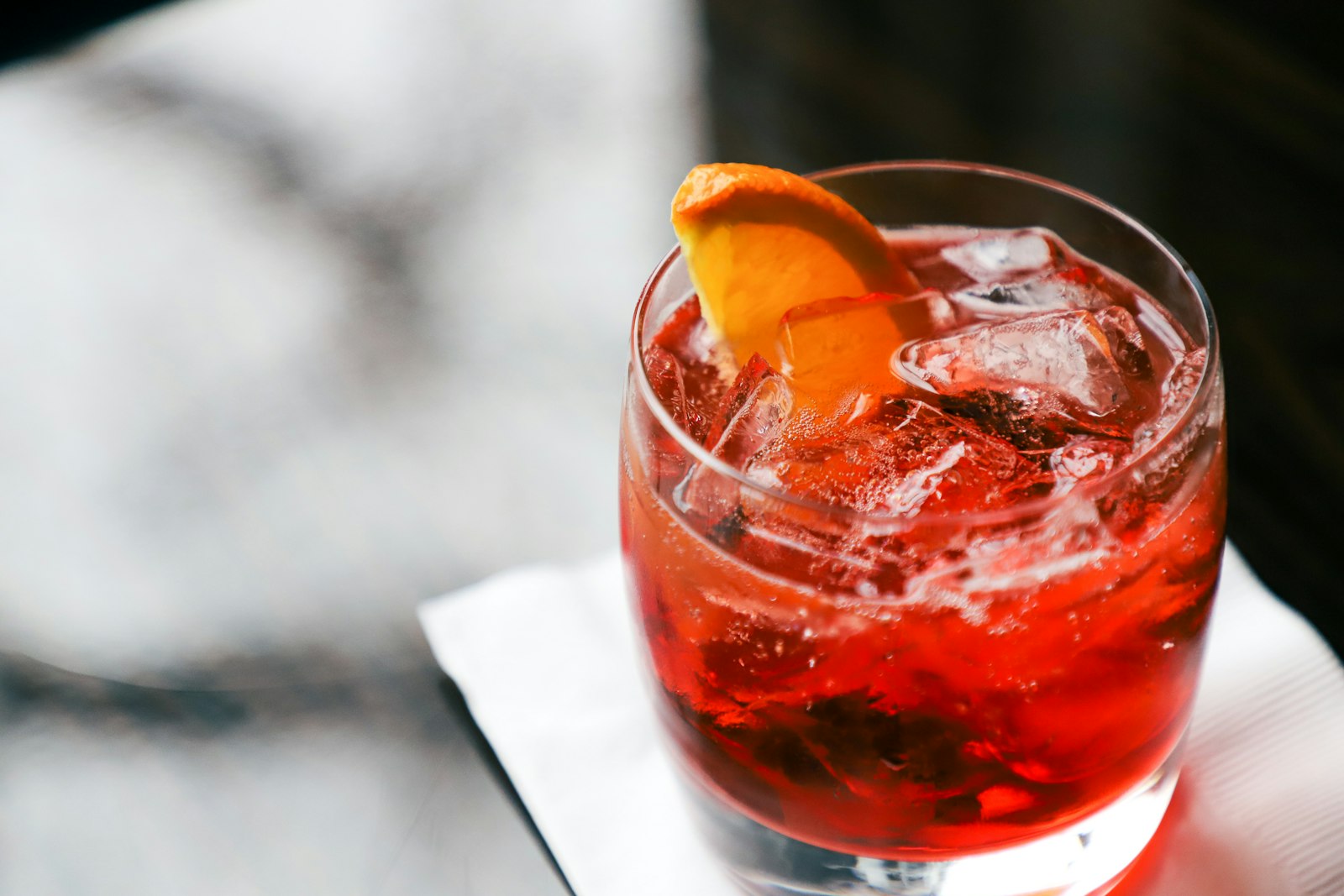 Deep red Blood Orange Negroni in a rocks glass with one large ice cube and a long orange peel