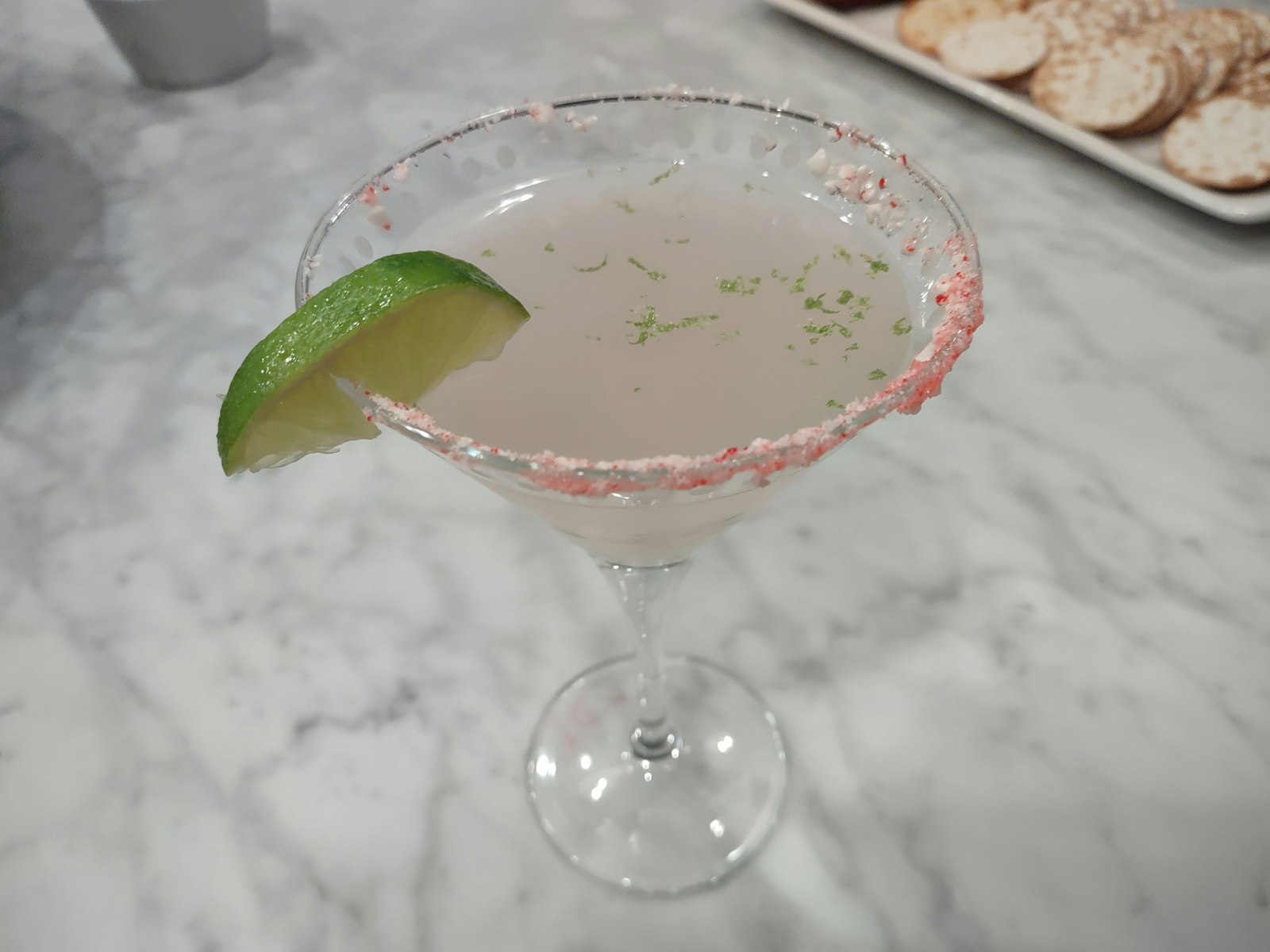 Bright pink Christmas Cosmopolitan in a coupe with sugared cranberries on a pick