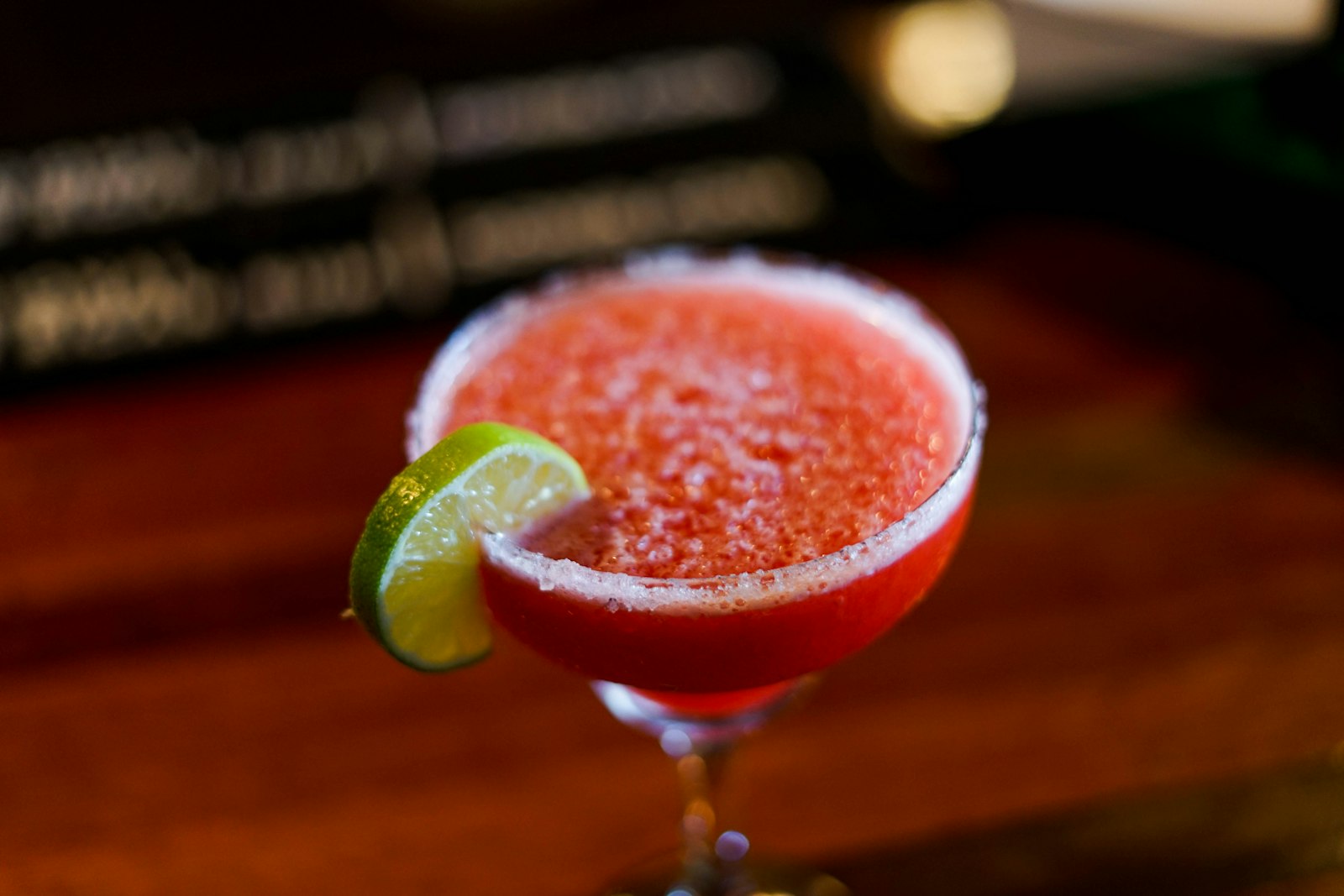 Christmas margarita in a coupe glass with cranberries and rosemary, salt-sugar rim glittering under warm light.