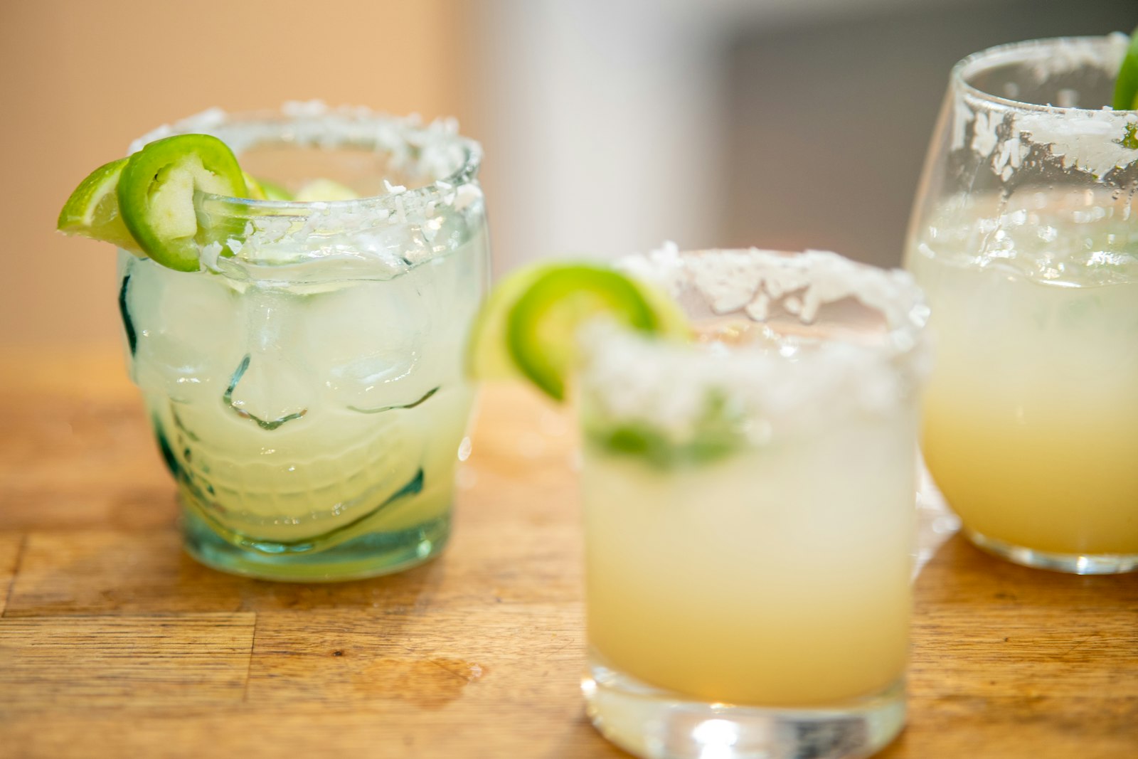 Cinnamon margarita in a rocks glass with a cinnamon-sugar rim, lime wheel and cinnamon stick garnish over a large ice cube.