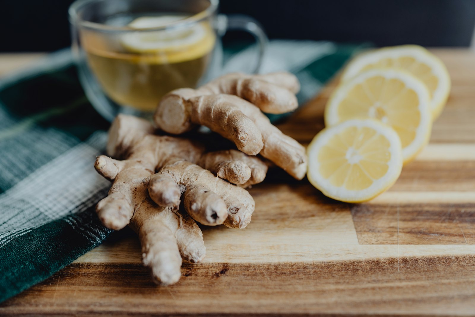 A heatproof glass of hot ginger and apple drink with lemon slices, ginger and a cinnamon stick.