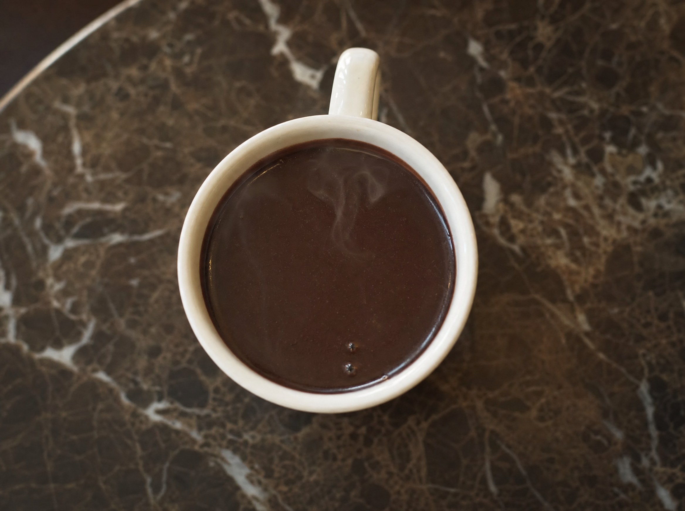 A heatproof mug of brandy hot chocolate topped with whipped cream and a dusting of cocoa.
