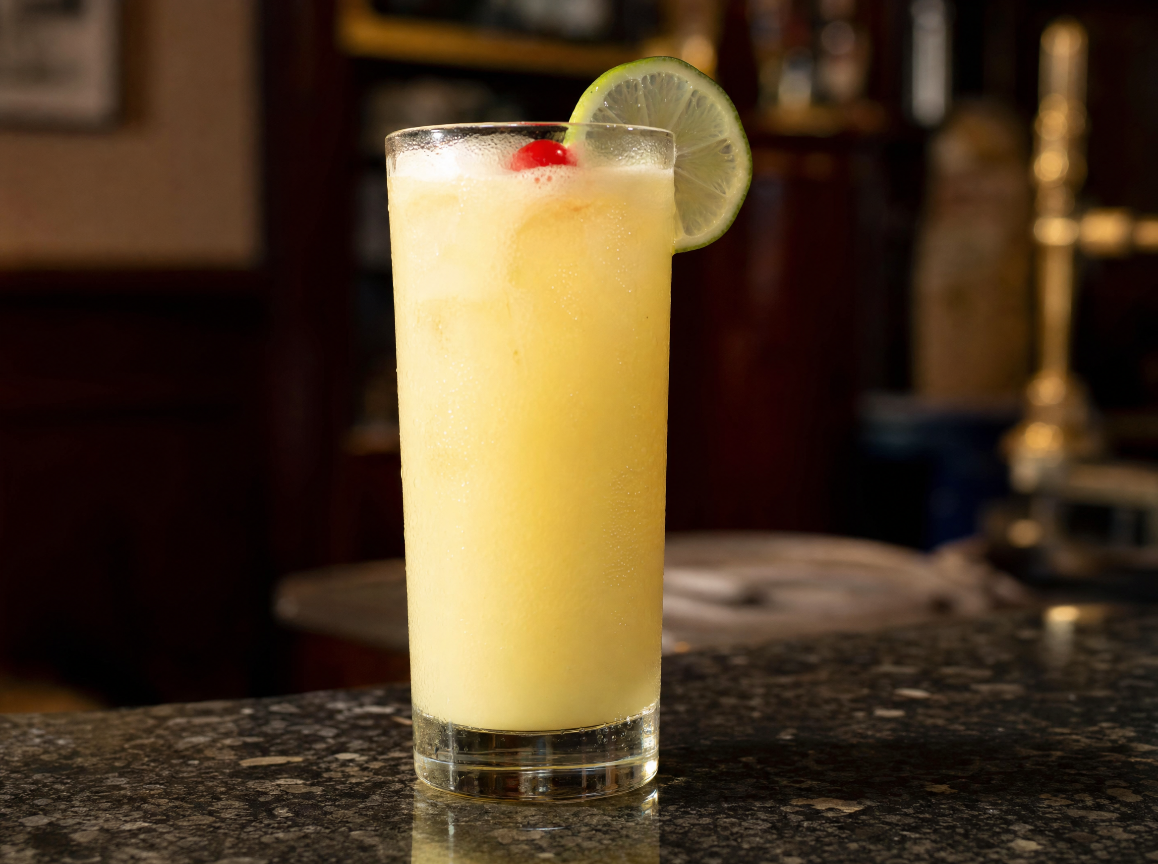 Highball glass of pale yellow snowball cocktail with a maraschino cherry