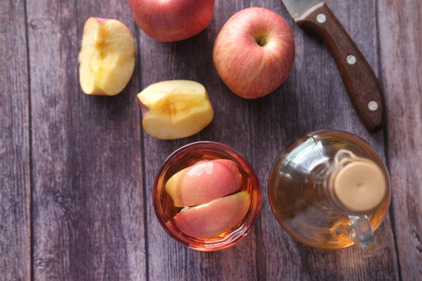 A heatproof mug of warm vanilla apple cider with a cinnamon stick and orange slice.